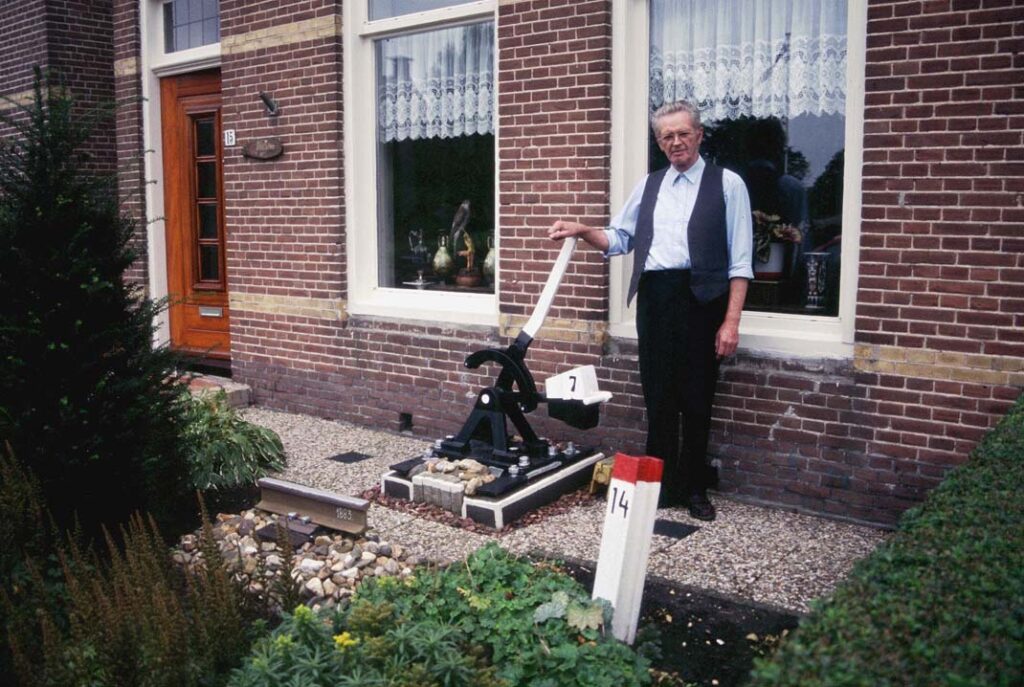 NFLS-kenner Wietse Hoekstra voor zijn huis in Minnertsga, oktober 2002. In de tuin tastbare herinneringen aan de NFLS, zoals een stuk rails, een kilometerpaal en een deel van een wissel uit Dokkum. Foto: Oege Kleijne.