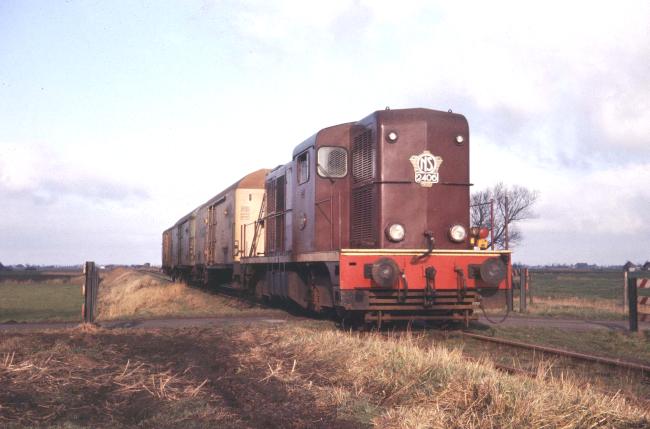 Loc 2406 met een korte goederentrein nabij Hijum, ten noorden van Stiens op de lijn naar Dokkum, november 1972. De koelwagens vervoerden aardappels die zonder koeling, maar wel beschermd tegen temperatuurschommelingen op hun buitenlandse bestemming moesten arriveren. Foto: Klaas Okkinga.